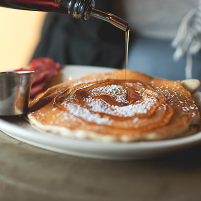 Pancakes with icing sugar and maple syrup being poured on top.